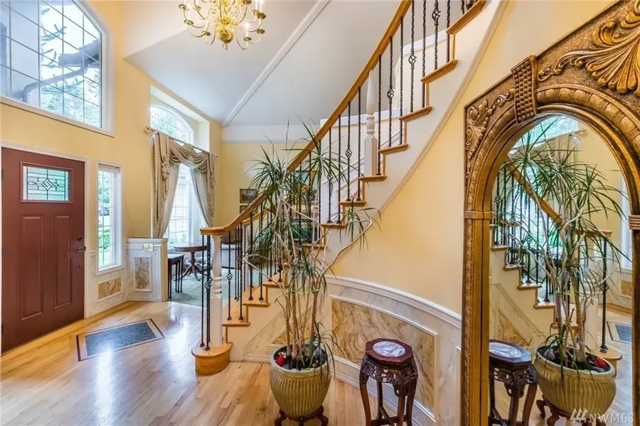 The entry foyer at A Rose Garden, a warm two-story space with a wood front door, a curved staircase, hardwood floors, and a chandelier in soft daylight