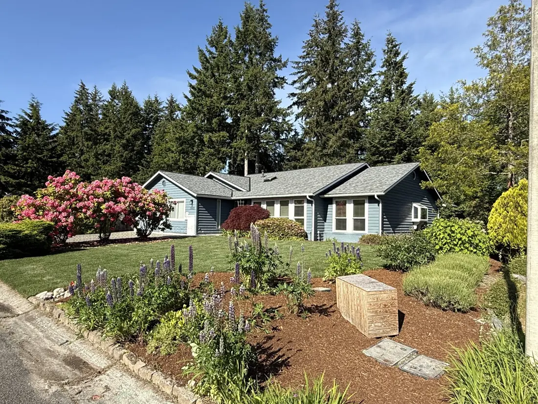 A Rose Garden Home 2 in Mill Creek, a blue craftsman house with a blooming front garden of rhododendrons and lupines